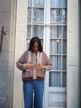 Sweater de punto a rayas horizontales blancas y azul marino, con cuello redondo, cierre frontal con botones y mangas largas con puños y detalles en tono azul.