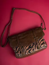 Bolso bandolera marrón con solapa superior de cuero sintético texturizado y cuerpo con estampado animal print de cebra.