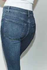 Jeans de tiro alto con corte skinny y largo tobillero. Presenta diseño clásico de cinco bolsillos, cierre frontal con cremallera y botón, con un acabado de lavado azul medio.
