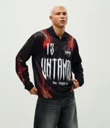 Remera de manga larga con corte boxy, confeccionada en microfibra de poliéster. Presenta un diseño estampado con motivos de llamas en tonos rojos y naranjas, junto con el número 13 en tipografía gótica en la espalda.