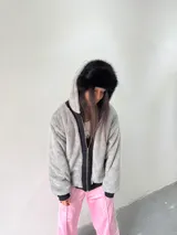Campera reversible con cierre frontal. Un lado es de algodón negro con estampa y bordado en color rosa, y el otro lado es de tela polar de pelo largo en color gris. Presenta corte oversize, capucha y puños acanalados.