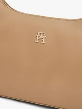Cartera tipo hobo de Tommy Hilfiger en color beige, con acabado liso, cierre de cremallera, asa superior y correa ajustable y extraíble. Cuenta con el logo metálico de la marca en relieve en la parte delantera.