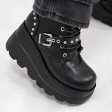 Botas de plataforma estilo borceguí, color negro, confeccionadas en materiales sintéticos. Presentan una suela de goma dentada, cordones frontales y una tira decorativa con hebilla metálica y tachas plateadas en la parte superior.