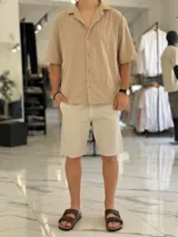 Camisa de lino color beige, de manga corta, con cuello abierto y cierre frontal de botones.