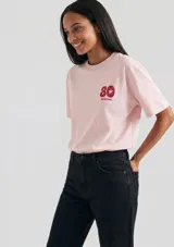 Remera de algodón color rosado, de corte clásico y manga corta, con cuello redondo acanalado y estampa frontal pequeña con el número 80 y el logo de la marca.