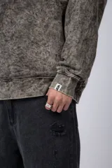 Buzo de cuello redondo con efecto de teñido artesanal acid wash. Presenta un corte oversize, mangas largas con puños acanalados y etiqueta pequeña en el puño izquierdo.