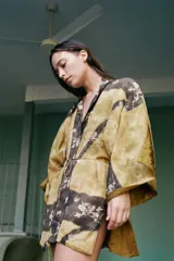 Kimono reversible de corte holgado con escote en pico y mangas anchas por debajo del codo. Un lado presenta un acabado texturizado en color bronce, mientras que el otro lado muestra un estampado floral sobre fondo oscuro. Incluye cierre frontal con lazada fina.