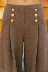 Pantalón de tiro alto con pierna ancha, confeccionado en sarga color tostado. Presenta detalle de doble hilera de botones metálicos dorados en el frente y pinzas verticales.