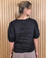 Blusa blanca de lino, con cuello redondo y mangas cortas abullonadas con frunces en los hombros.