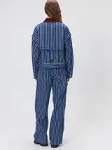 Campera de denim a rayas verticales con cuello de pana en color bordó. Presenta cierre frontal, mangas desmontables con cierre en los hombros, canesú en el pecho y bolsillos de parche cuadrados.