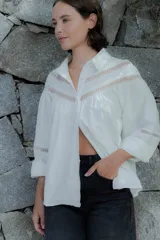 Camisa de algodón color beige con detalles de encaje y broderie en el canesú y las mangas. Presenta cuello camisero, cierre frontal con botones y mangas largas con puños.