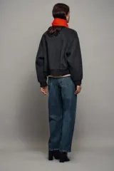 Cazadora bomber beige confeccionada en hilatura con lana, con cuello subido, manga larga y bolsillos frontales. Presenta cierre frontal con botones oscuros y puños, cuello y ruedo en tejido rib.