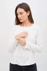 Remera de manga larga color blanco, confeccionada en tejido suave con textura acanalada. Presenta volados verticales decorativos en el frente y en los puños, con un calce cómodo y favorecedor.