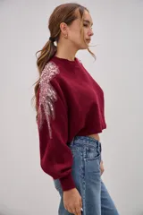 Sweater de punto color bordó, de corte cropped y mangas largas con puños ajustados. Presenta detalles decorativos de apliques bordados con lentejuelas y perlas en la zona de los hombros.