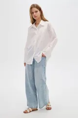 Camisa de algodón blanca, de corte oversize, manga larga y cuello camisero, decorada con apliques de strass y bordados sutiles en la parte delantera.