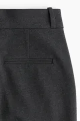 Pantalón sastrero de tiro alto con corte recto, cierre frontal con botón oculto y corchetes, bolsillos laterales al bies y pliegues marcados en el frente y la parte posterior.