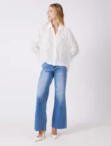 Camisa de gasa ligera y traslúcida, color blanco, con intrincados bordados búlgaros y motivos botánicos distribuidos en toda la prenda. Presenta una guarda bordada que recorre la línea de botones, el ruedo y los puños. Tiene cuello con solapa y abertura central con botones. La silueta es amplia y relajada, con mangas largas y un canesú en la espalda para una caída impecable.