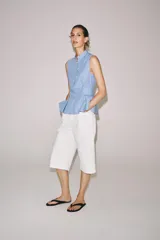 Camisa sin mangas de algodón con rayas verticales blancas y azules, cuello mao, bajo acabado en peplum y cierre frontal con alamares decorativos de nudo.