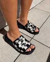 Zueco de mujer con plataforma y taco bajo, color marrón oscuro. La capellada es de tiras trenzadas en patrón damero (cuadros) en tonos marrón oscuro y blanco/beige.