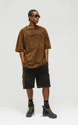 Bermuda cargo de algodón rústico, color marrón oscuro con efecto desgastado (acid wash/oxidado). Presenta un calce oversize, cintura elástica y grandes bolsillos laterales con tapa.