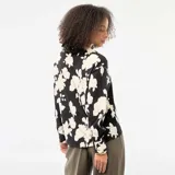 Blusa de corte fluido con estampado floral en contraste, cuello camisero, cierre frontal de botones y mangas tres cuartos.