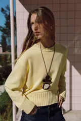 Sweater de punto color amarillo claro, con cuello redondo, manga larga y dobladillo asimétrico más largo en la parte trasera. Presenta acabados en rib en cuello, puños y ruedo.