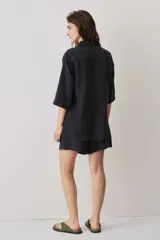 Camisa negra de manga corta, con cuello camisero, cierre frontal de botones y un bolsillo aplicado en el pecho.