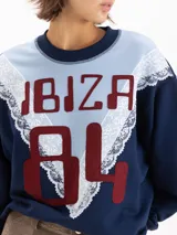 Buzo de cuello redondo en color rosado, con un diseño combinado en el pecho que incluye un panel superior bordó, detalles de encaje y la inscripción "IBIZA 84" en tono beige.