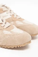 Championes deportivos en tonos beige y ocre, confeccionados con combinaciones de materiales texturados y forro interior de corderito sintético. Presentan suela dentada de goma que se extiende hacia el talón.