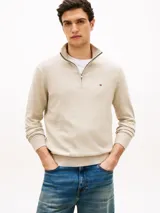 Sweater de punto color beige con cuello perkins, cierre frontal con cremallera corta y manga larga. Presenta detalles de rib en cuello, puños y dobladillo, además del logo bordado en el pecho de Tommy Hilfiger.