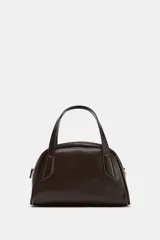 Bolso de mano y bandolera color marrón oscuro, con forma redondeada y doble asa superior. Presenta cierre principal de cremallera y un bolsillo interior con cierre.