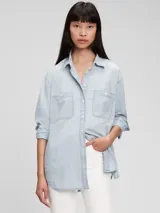 Camisa oversize de jean celeste claro, con cuello clásico, cierre frontal con botones a presión, dos bolsillos con solapa en el pecho y mangas largas con puños abotonados.