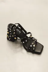 Sandalias de tacón ancho de 7 cm, color bordó, con diseño de tiras cruzadas en el empeine y pulsera al tobillo con cierre de hebilla. El modelo está decorado con tachas metálicas plateadas y doradas distribuidas por todas las tiras y el tacón.