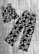 Conjunto de chaleco y pantalón palazzo negro con estampado floral blanco. El chaleco es corto y abotonado, mientras que el pantalón es de corte amplio y tiro alto.