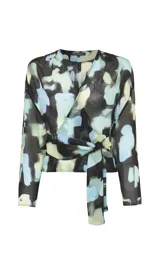 Blusa de tejido fluido con estampado abstracto en tonos azules, negros y beige. Presenta un diseño cruzado con escote en V, mangas 3/4 anchas y un lazo lateral ajustable que define la silueta.