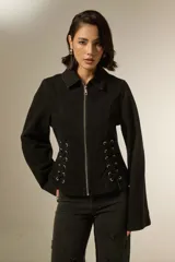 Sobrecamisa de jean color negro, con cierre frontal y detalles de cordones laterales ajustables con ojales metálicos. Presenta cuello clásico y mangas largas.