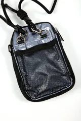 Cartera bandolera pequeña color dorado metálico, con cierre principal y bolsillo frontal con cierre. Tiene una correa ajustable de cordón negro y un parche rectangular negro con el logo "IND" en blanco.