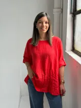 Blusa roja de lino, con cuello redondo, mangas 3/4 con presilla y botones, y diseño holgado con pliegues frontales.