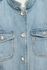 Cazadora de denim de corte entallado, color celeste, con cuello subido, manga larga y cierre frontal con botones metálicos. Cuenta con bolsillos con solapa en el pecho y en la parte inferior delantera, además de presillas en los hombros.