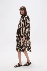 Vestido tipo camisa de corte holgado, con estampado de hojas en tonos marrones y beige. Presenta cuello camisero, cierre frontal con botones y mangas largas.