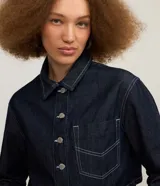 Camisa de jean estilo cropped de color azul oscuro, con cuello inglés, mangas largas, cierre frontal de botones metálicos y un bolsillo aplicado en el pecho. Cuenta con costuras pespunteadas en tono contrastante.