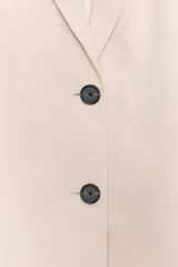 Blazer de mujer color beige claro, corte oversize, con cuello solapa, manga larga y cierre frontal de dos botones. Presenta bolsillos de vivo con solapa en el delantero.