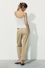 Pantalón chino color beige de tiro medio con bolsillos frontales y falsos bolsillos de vivo en la espalda. El bajo tiene un acabado con vuelta. Incluye un cinturón trenzado marrón.