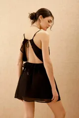 Vestido corto negro de viscosa georgette, con escote en V, volados en el frente y espalda descubierta. Cuenta con breteles finos ajustables que se atan en la espalda y ajuste elástico en la cintura.