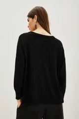 Sweater de punto negro con cuello redondo y mangas largas. Presenta un detalle bordado con lentejuelas en forma de hojas y flores en el hombro derecho.