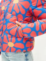 Campera puffer corta con estampado abstracto en tonos verde, naranja y azul. Tiene cuello alto, cierre frontal con cremallera y bolsillos laterales.