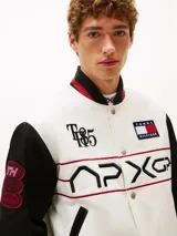 Campera estilo universitario de Tommy Hilfiger, colección APXGP, color blanco con mangas negras y detalles en rojo. Confeccionada en satén aterciopelado, con cuello estilo béisbol, cierre a presión, bolsillos laterales ribeteados, cuello, puños y bajo de punto canalé con rayas, logo de la colección APXGP bordado en la parte delantera y parches con el logo de la colección APXGP en mangas.