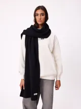 Bufanda de tejido de punto grueso en color negro, con etiqueta de la marca Rusty en uno de los extremos.