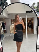 Pollera corta de cuero sintético con diseño de paneles y bolsillos frontales grandes. Presenta un corte recto y tiro medio.