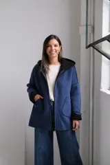 Tapado de paño azul con capucha, diseño de corte holgado y largo a la cadera. Presenta detalles en color negro en el interior, bordes y puños, con bolsillos frontales amplios y cierre frontal.